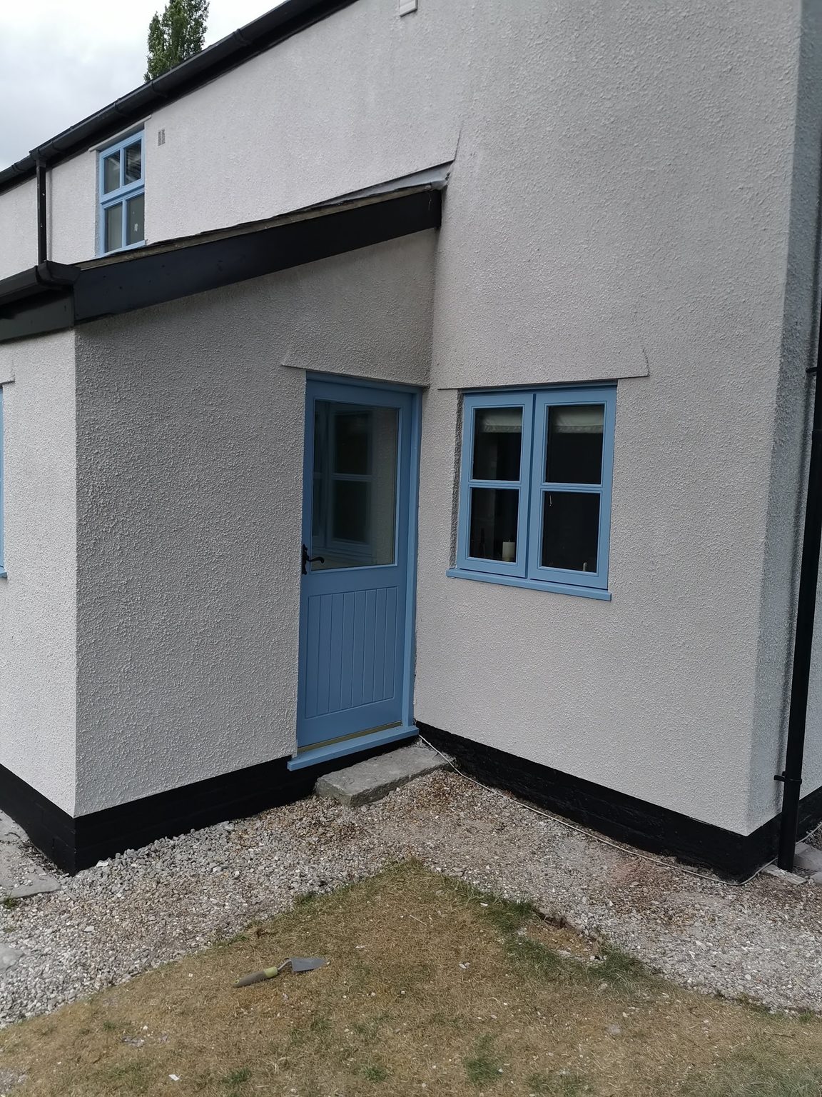 Cottage with a smooth white render finish, black plinth and a blue stable door