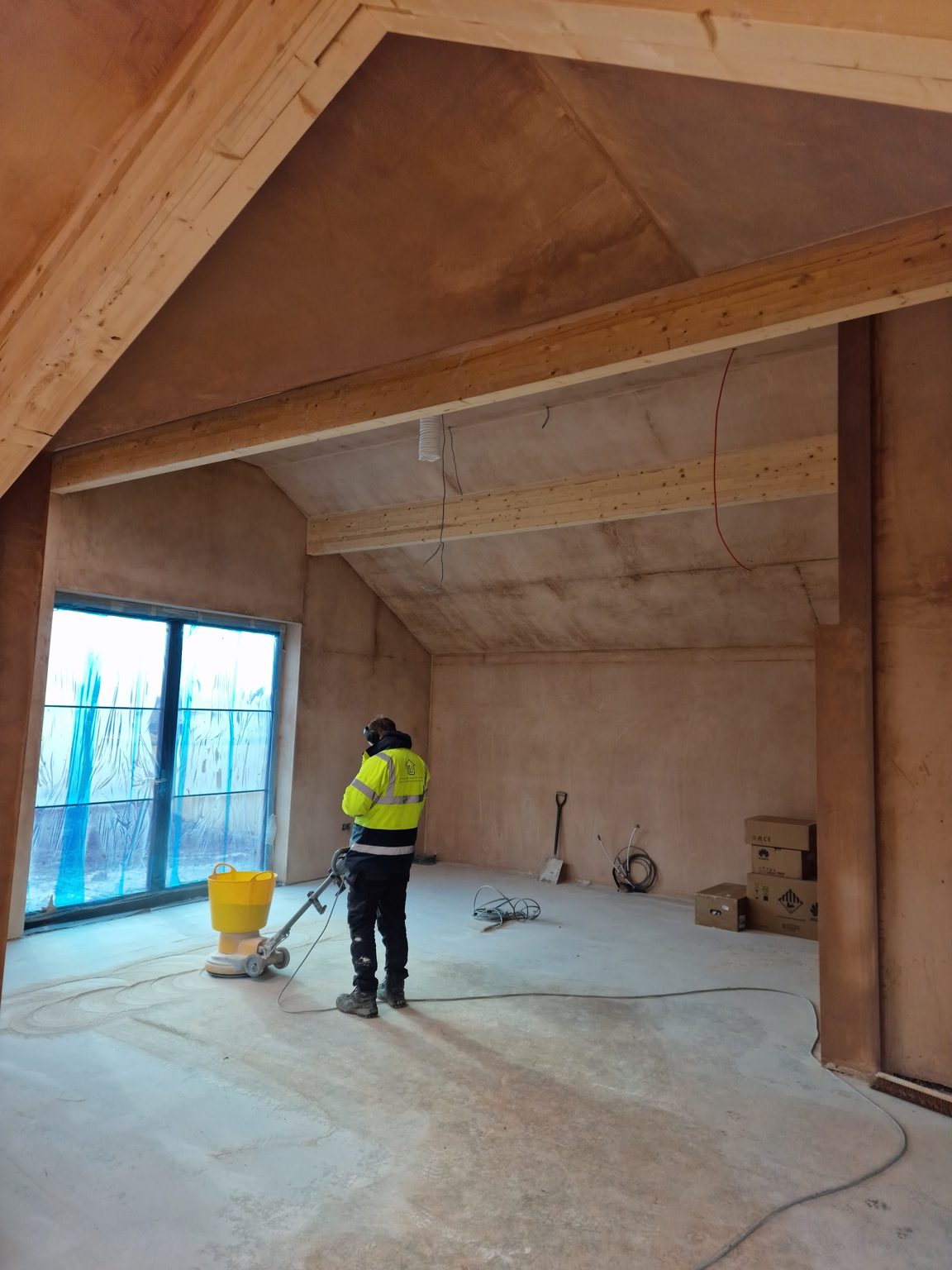 Plasterer in hi-vis preparing the floor of a new vaulted extension with plastered walls